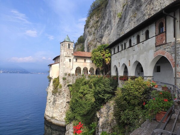A historic building with a tower and arched windows, situated on a cliff overlooking a body of water.