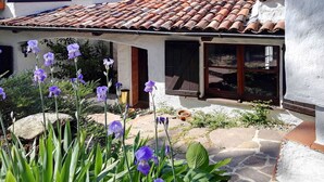 Una casa con techo de tejas, un camino de piedra y flores moradas al frente.