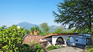 Una casa rural con techo de tejas, un camino de piedra y montañas al fondo.