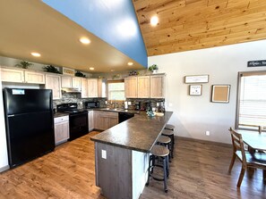 A modern kitchen with wooden cabinets, a black refrigerator, a microwave, and a central island with bar stools.