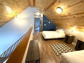 Une chambre avec un plafond en pente, un lit, une table de chevet, un tapis et un petit meuble.