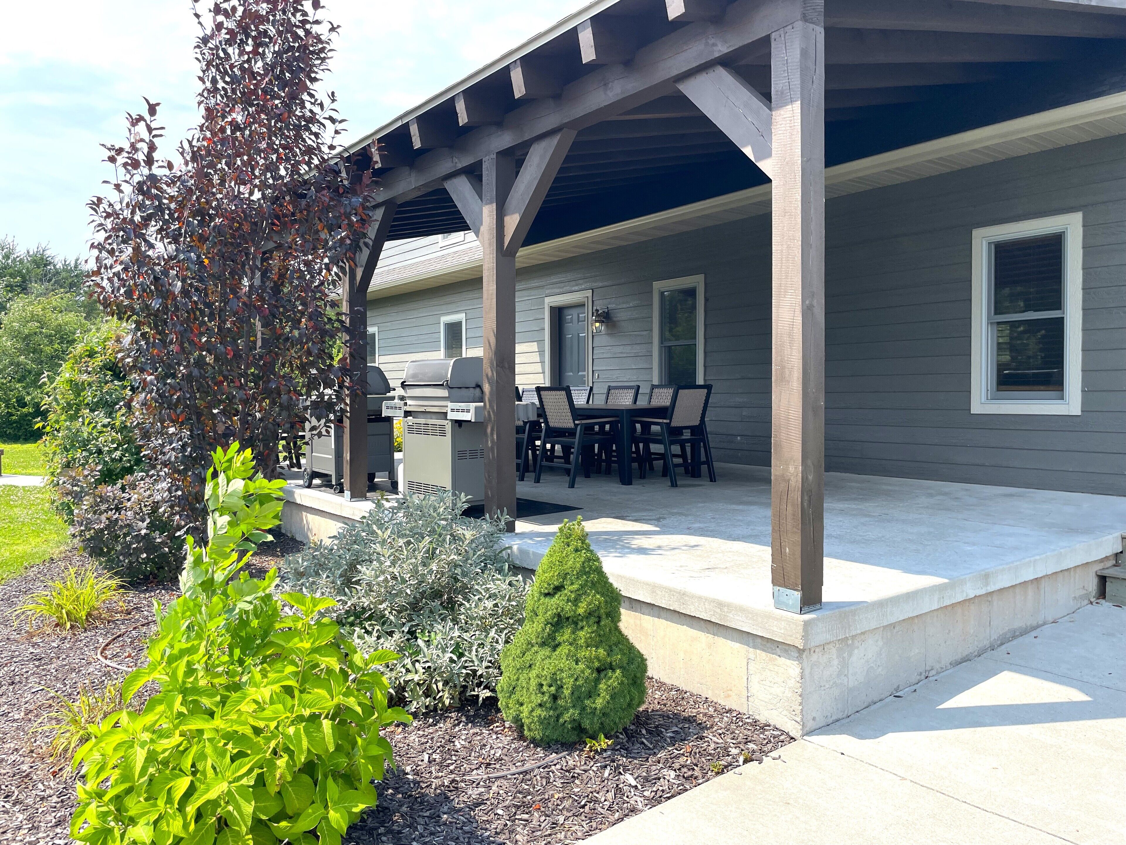 Un patio couvert avec un barbecue, des meubles d’extérieur et un jardin bien entretenu.