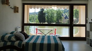 A room with a bed, a table, and chairs by a large window overlooking a scenic landscape. - Comfortable studio with view of pond and Chateau (Chauffailles)