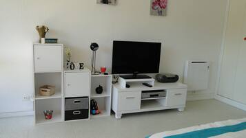 Un dormitorio con cama, televisor, un armario blanco y una pequeña estantería con adornos.