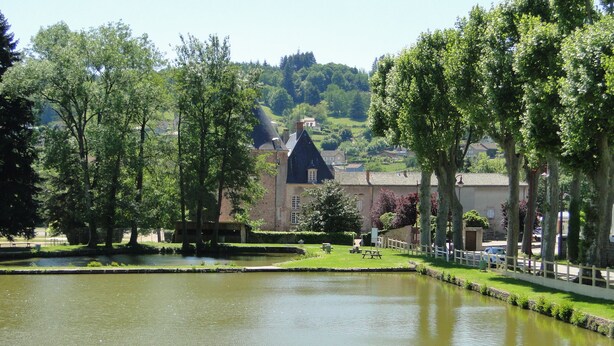 A serene riverside view with a historic building, a picnic table, and a white fence along the water's edge. - Comfortable studio with view of pond and Chateau (Chauffailles)