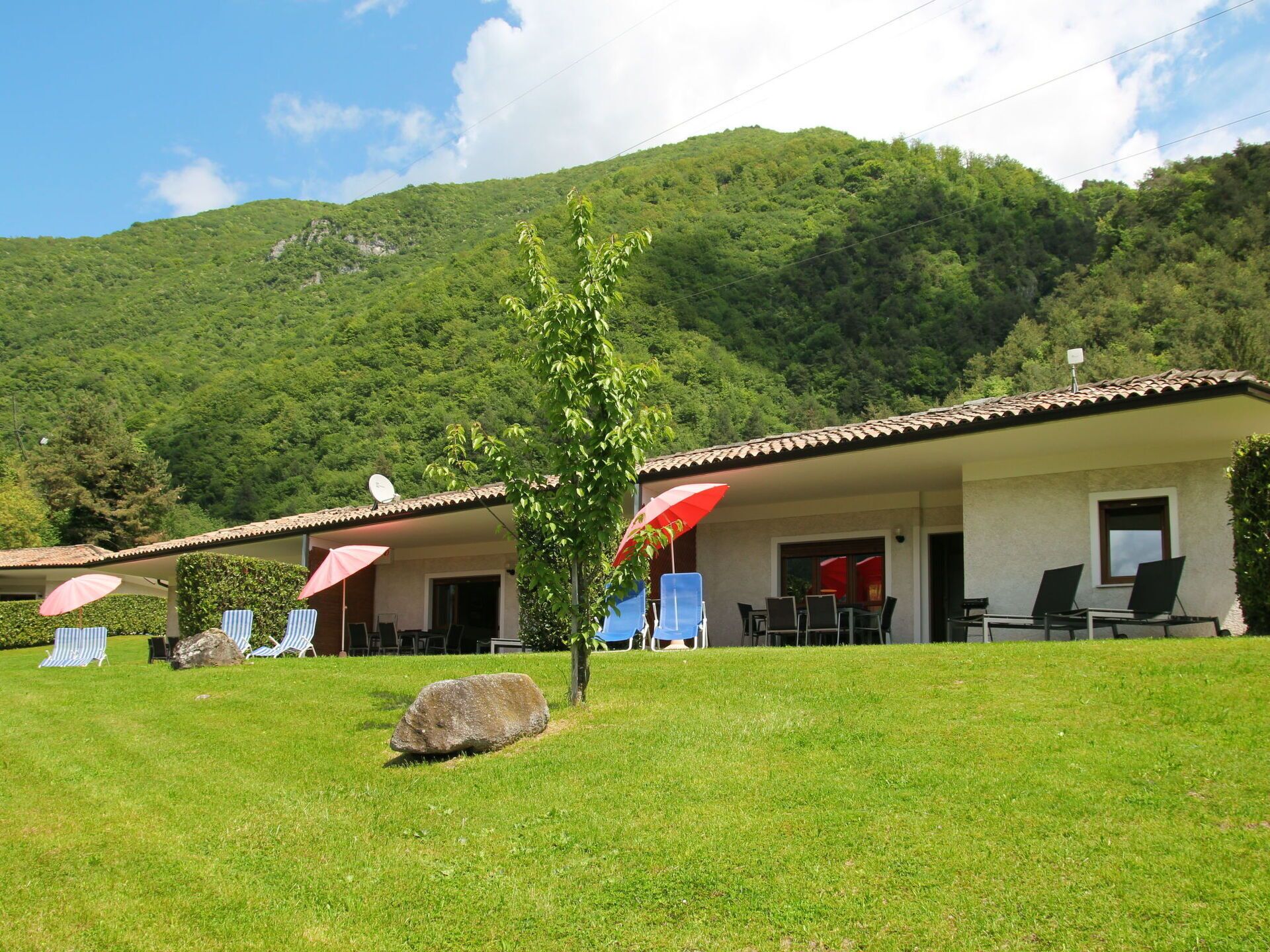 A hotel with outdoor seating, a small tree, and a mountain backdrop.