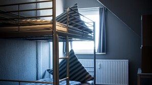 Una camera del dormitorio con letti a castello, una finestra con tende, un termosifone e un pavimento in legno.