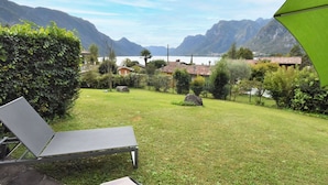Un espace extérieur verdoyant, avec une table et des chaises, entouré de végétation et offrant une vue sur les montagnes et un lac.