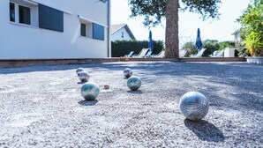 Un cortile con fondo in ghiaia, un albero e poltrone da relax sotto ombrelloni.