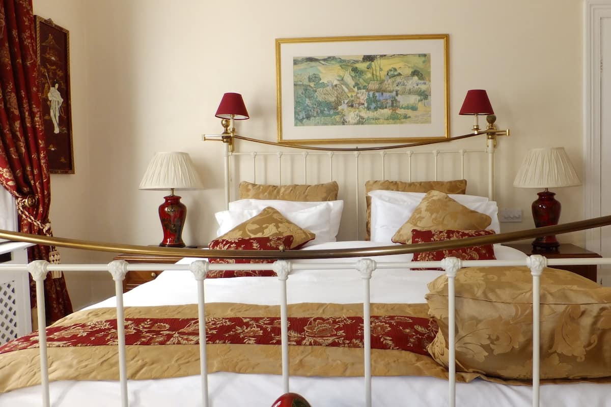 Un dormitorio ordenado con una cama, dos mesitas de noche, un cuadro en la pared y una puerta al fondo.