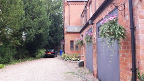 A gravel driveway leading to a brick building with hanging flower baskets. - Garfits lodge (Boston)