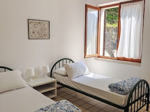A single bed with a white mattress and a patterned blanket, a bedside table with a lamp, and a window with curtains. - Lovely apartment for 6 people with WIFI, TV, terrace and pets allowed (Crone)