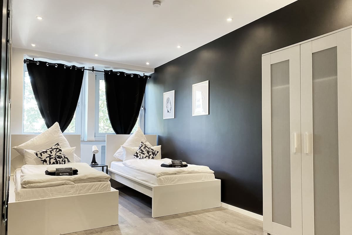 A modern hotel room with two beds, a wardrobe, and a window with curtains.