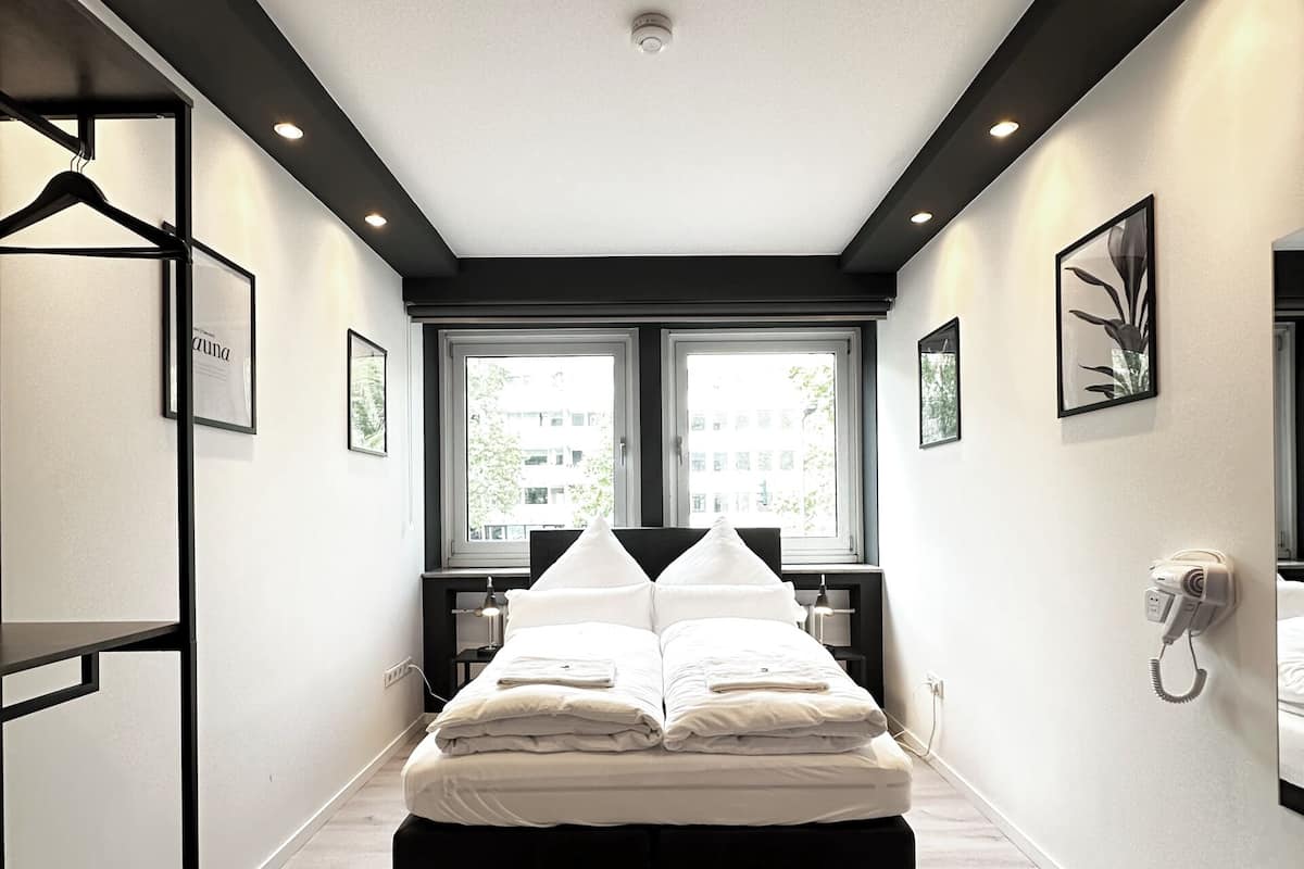 A modern bedroom with a bed centered in the room, flanked by windows, a wall-mounted phone, and framed pictures.