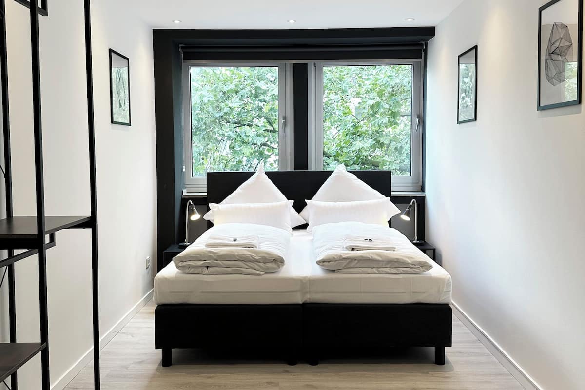 A modern bedroom with a large bed, two windows, and a view of trees.