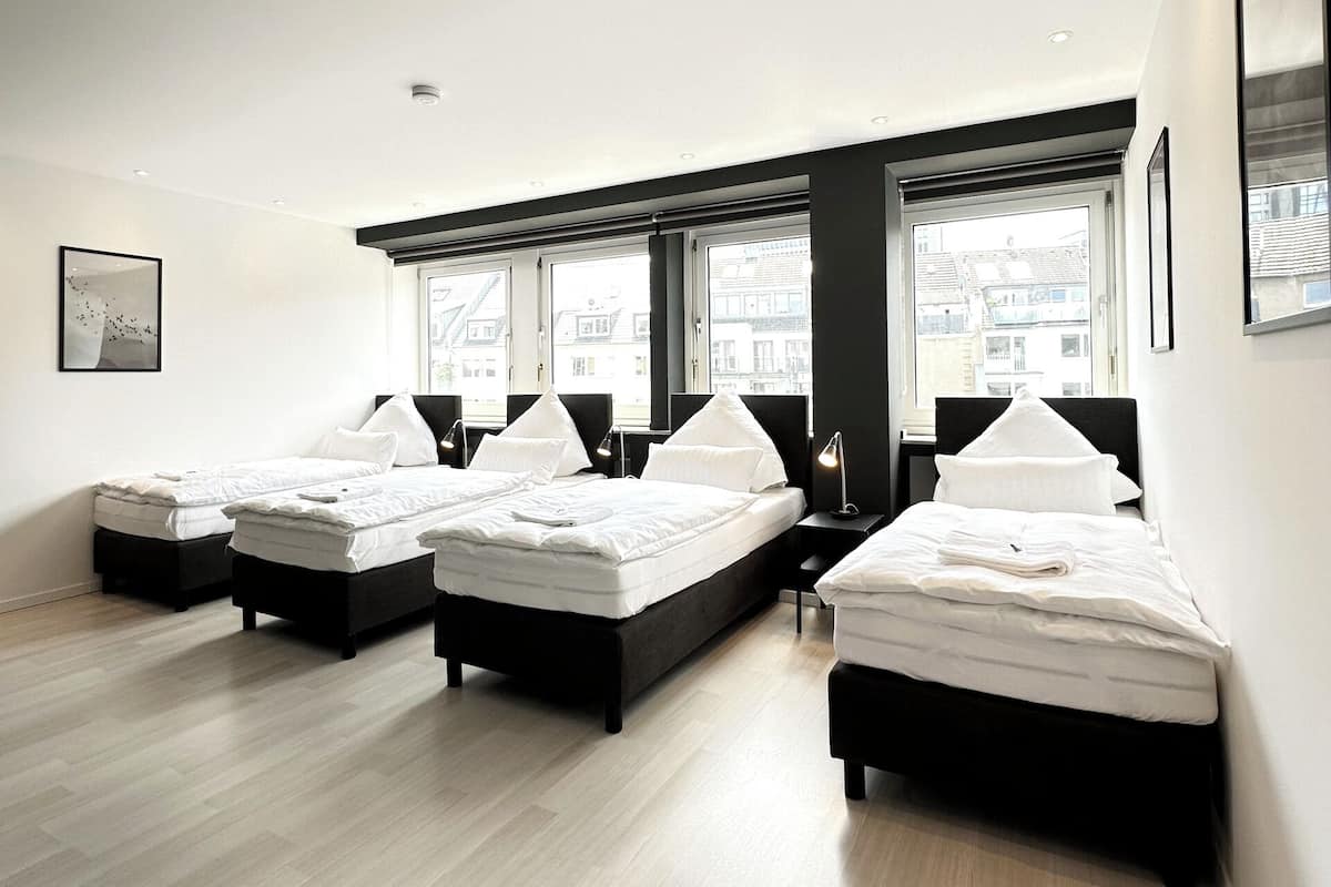 A modern hotel room with three beds, large windows, and a minimalist design.