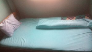 A single bed with a light blue mattress and pillows, a wooden headboard, and a patterned wall. - Twiga Guest House (Thika)