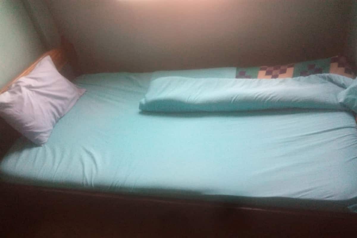 A single bed with a light blue mattress and pillows, a wooden headboard, and a patterned wall.