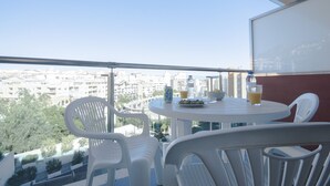 Un balcon avec des chaises en plastique blanches, une table ronde et une bouteille d’eau.