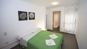 Une chambre d’hôtel avec un lit simple, une couvre-lit verte, deux serviettes blanches, un oreiller blanc et deux tableaux accrochés au mur.