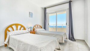 Ein Zimmer mit zwei Betten, einem Nachttisch, einer Lampe, einem Bild und Meerblick.