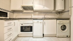 Eine kleine Küche mit weißen Schränken, einer Mikrowelle, einem Backofen, einem Geschirrspüler und einer Waschmaschine.
