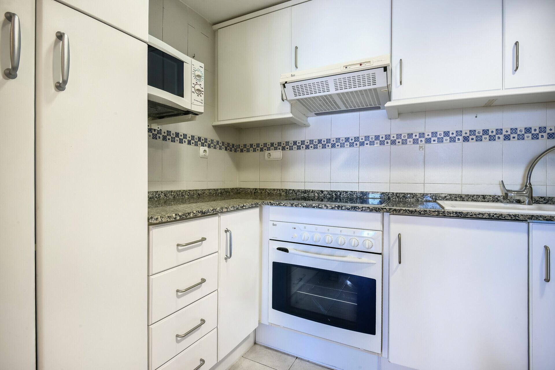A kitchen with white cabinets, a microwave, an oven, a sink, and a patterned backsplash.