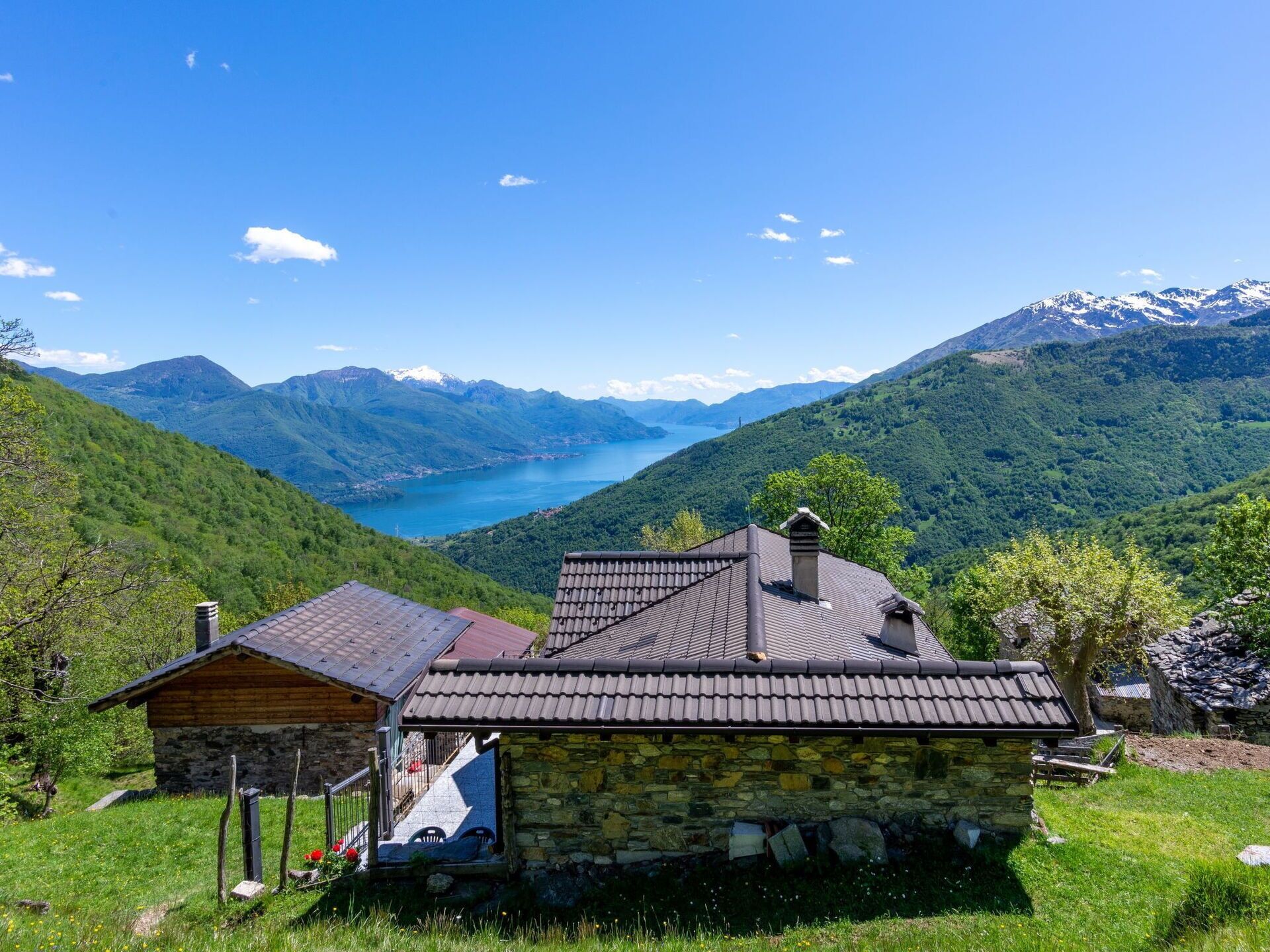 Uma casa de pedra com telhado de cerâmica, rodeada por vegetação exuberante e um cenário montanhoso.