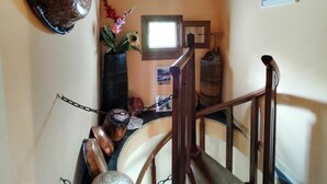 A staircase with a wooden handrail, a metal chain barrier, and a rustic decor including a wooden barrel and a vase with flowers.