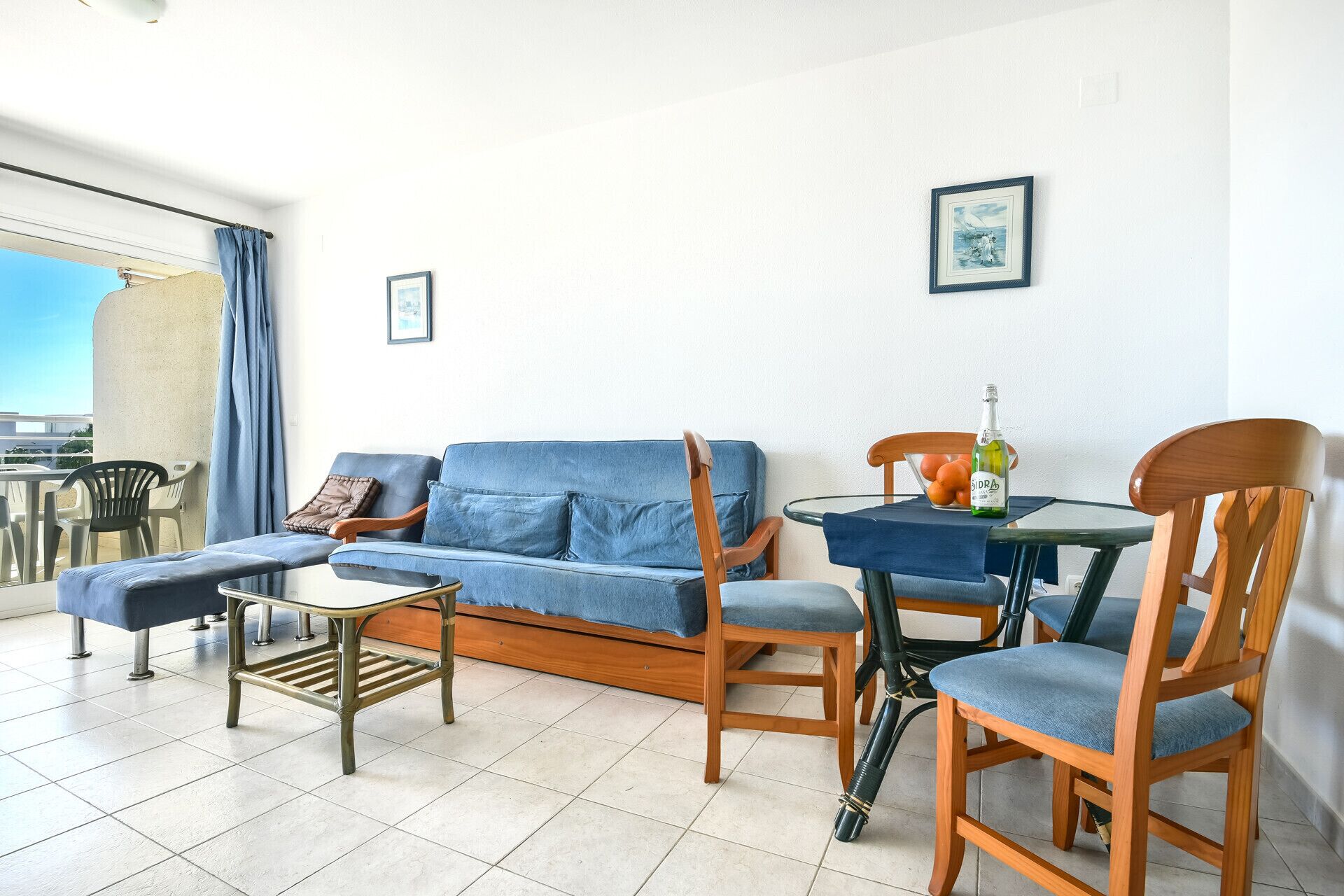 Ein Wohnzimmer mit einem blauen Sofa, Holzstühlen, einem kleinen Tisch und einem Balkon mit Aussicht.