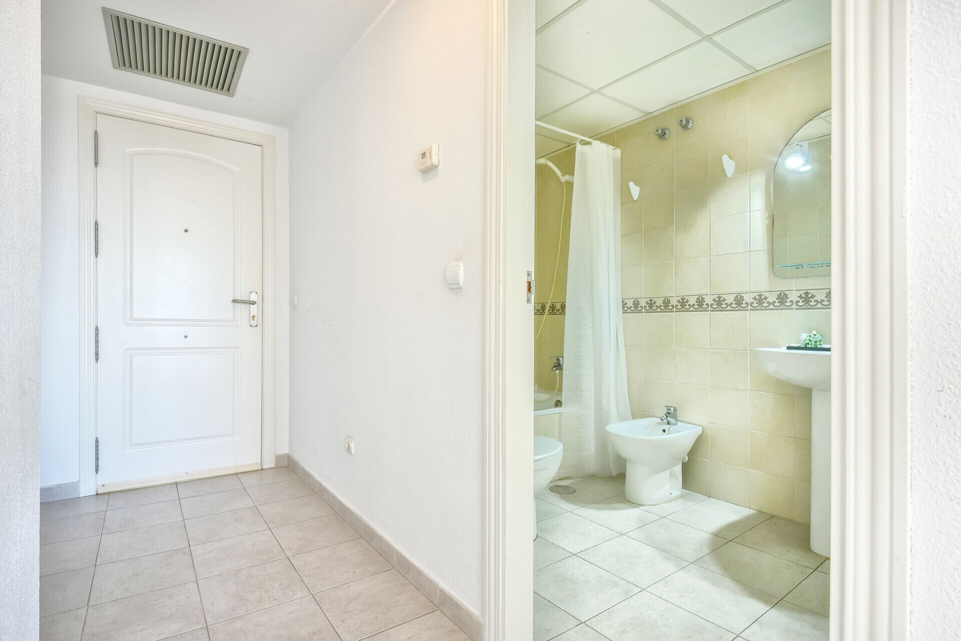 A hallway leading to a bathroom with a toilet, bidet, and sink.