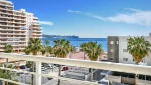 Un balcon avec vue sur la mer, des palmiers et un espace de stationnement.