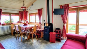 Uma sala de estar acolhedora com um sofá vermelho, uma mesa de jantar com cadeiras, uma lareira e uma TV fixada na parede.