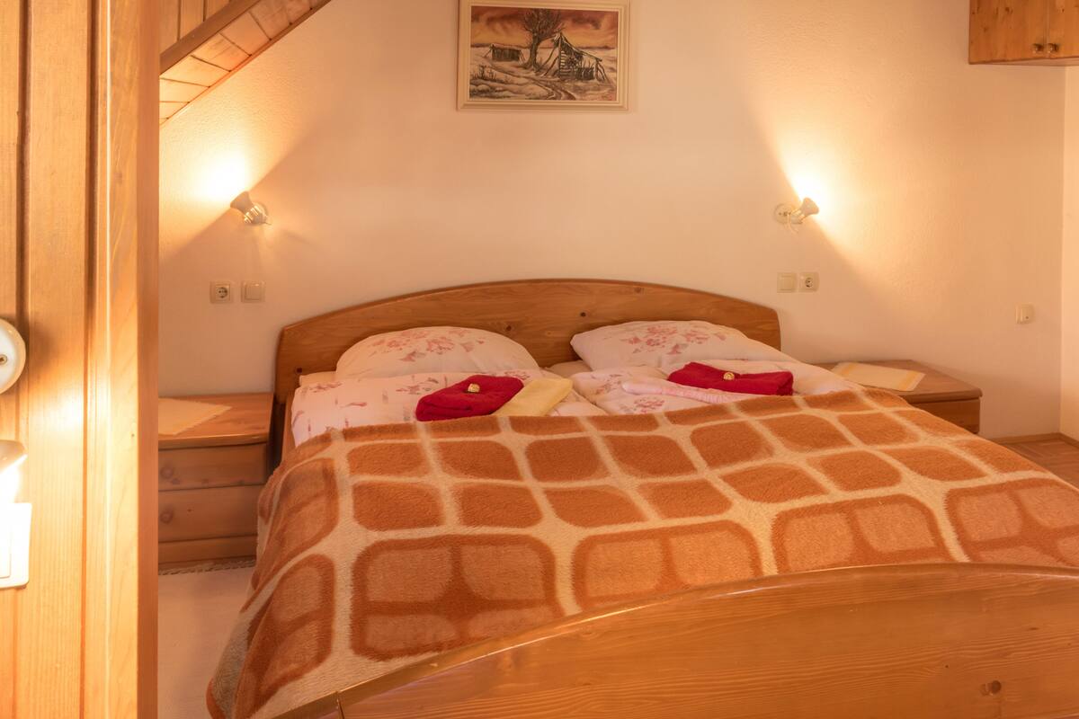 Un dormitorio con una cama de madera, dos mesitas de noche, una mesita auxiliar, una lámpara de pared y un cuadro sobre la cama.