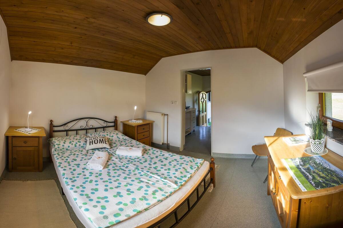 Un dormitorio con cama, cabecera de madera, mesitas de noche, un escritorio y una ventana.