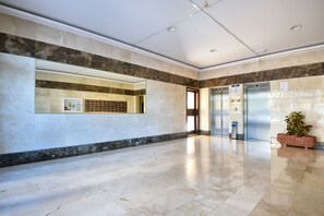 Un vestíbul ampli amb terra de marbre, una taula d'informació i un ascensor.
