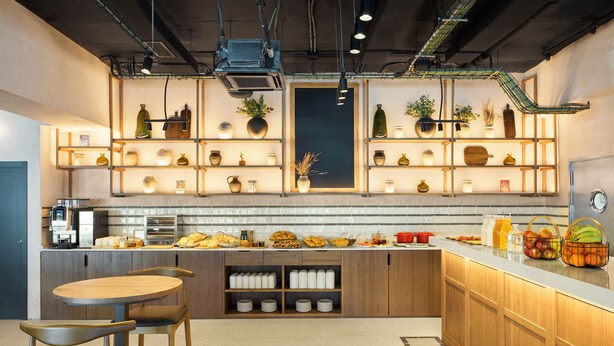 A modern kitchen with wooden cabinets, a central island, and a variety of kitchenware and plants on shelves.