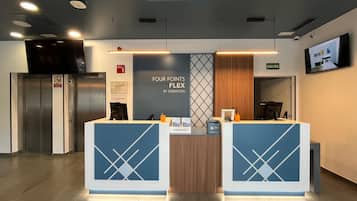 Ein Empfangsschalter mit einem Schild, auf dem 'FOUR POINTS FLEX BY SHERATON' steht, und ein Aufzug zur Linken.