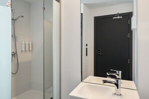 Un baño moderno con cabina de ducha de vidrio, un lavamanos blanco con accesorios cromados y una puerta negra.