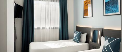 A hotel room with two beds, a TV, a window with curtains, and framed pictures on the wall.
