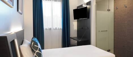 Een moderne hotelkamer met een bed, een aan de muur bevestigde televisie, een douche en een raam met gordijnen.