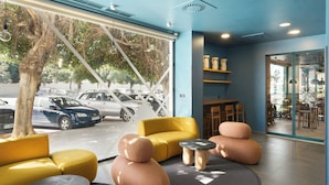 A modern interior with a yellow sofa, round tables, and a glass wall offering a view of parked cars outside.
