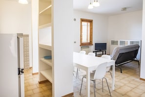 A room with a white table, chairs, a TV, a radiator, and a window.