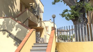 A building with a staircase, a tree, and a fence.