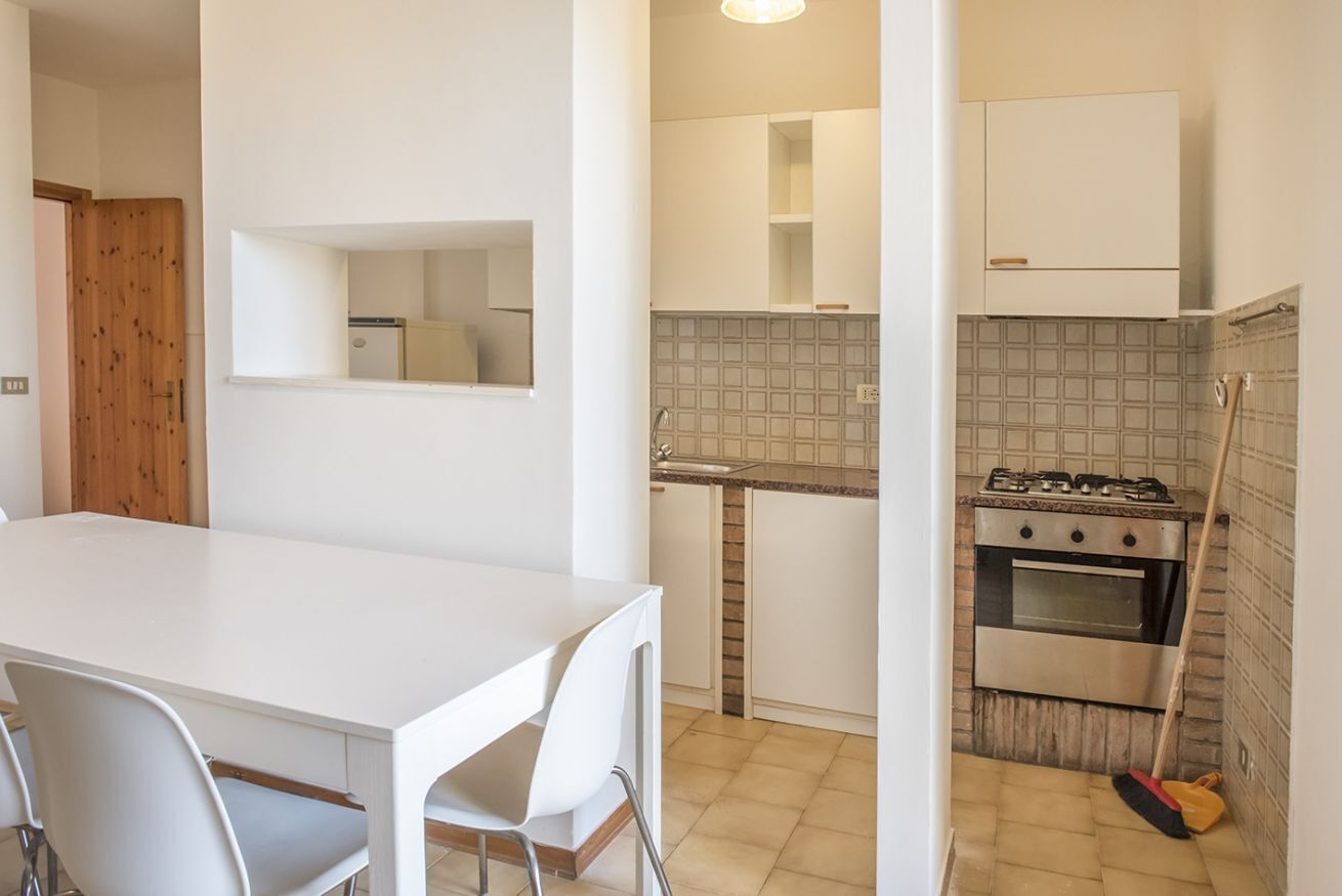 A kitchen with white cabinets, a stove, and a broom.