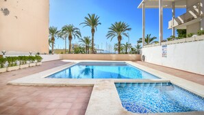 Une piscine dotée d’une terrasse carrelée, entourée de palmiers et surplombée par un ciel bleu azur.
