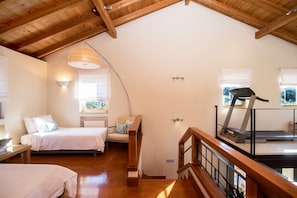 A bedroom with two beds, a treadmill, and a wooden ceiling.