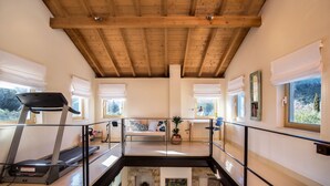 A spacious room with a wooden ceiling, a treadmill, a bench, and a view of the outdoors. - Villa Lithia Ano Korakiana (Ano Korakiana)