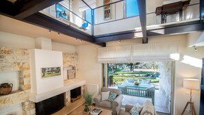 A spacious living area with a fireplace, a sofa set, and a view of the garden through large windows. - Villa Lithia Ano Korakiana (Ano Korakiana)