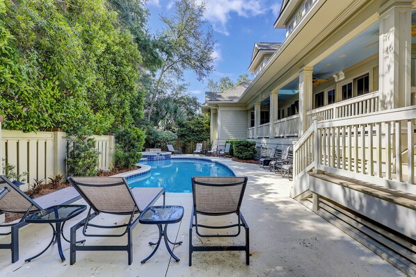 Un espace piscine doté de chaises longues et d’un jacuzzi, entouré de verdure et bordé d’un bâtiment avec un balcon.